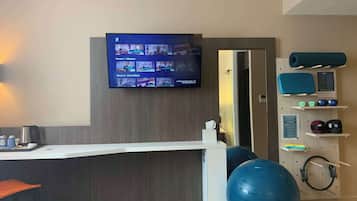 Un gimnasio con equipo de ejercicio, una televisión mostrando videos de entrenamiento y un mostrador de recepción.