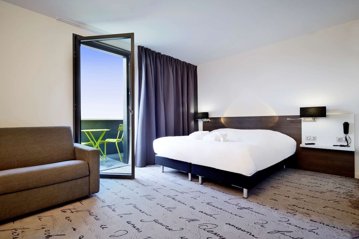 A hotel room with a bed, a sofa, a sliding glass door, and a view of the outdoors.