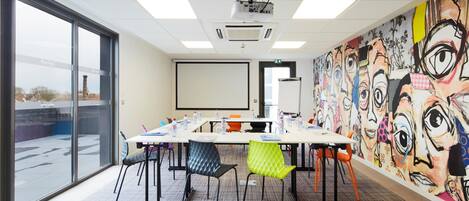 A conference room with a large table, chairs, a projector, and a mural on the wall.