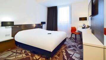 Une chambre d’hôtel avec un grand lit, un bureau, une chaise, une télévision et une fenêtre avec des rideaux.