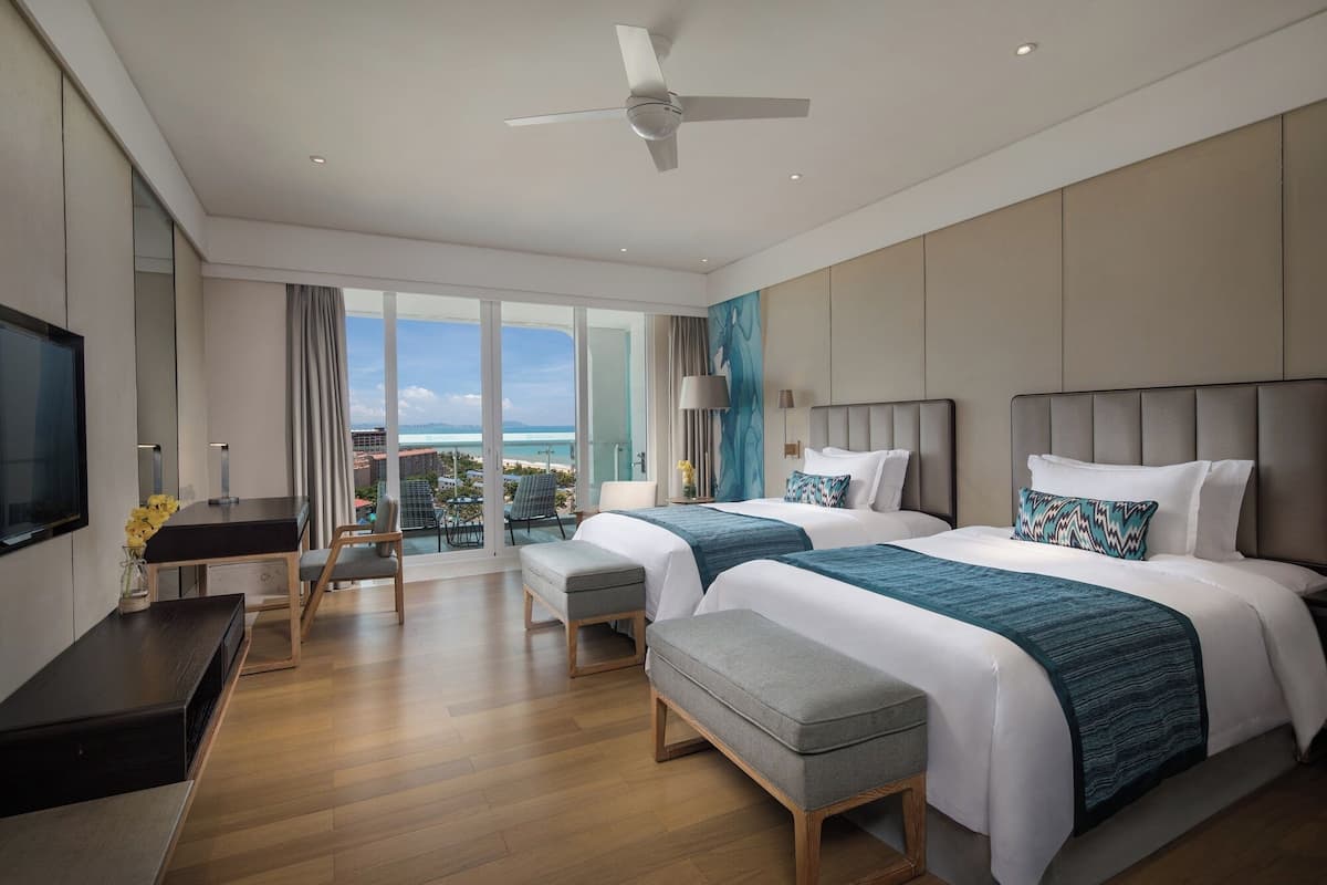 Une chambre d’hôtel moderne avec deux lits, une télévision, un bureau et un balcon offrant une vue sur l’océan.