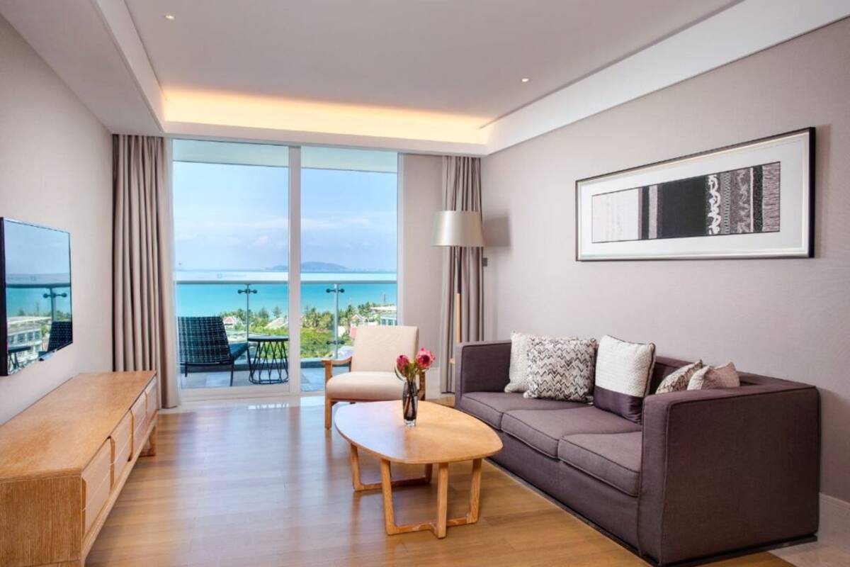 Un salon moderne avec un canapé, une table basse et un téléviseur. Une grande fenêtre offre une vue sur la mer.
