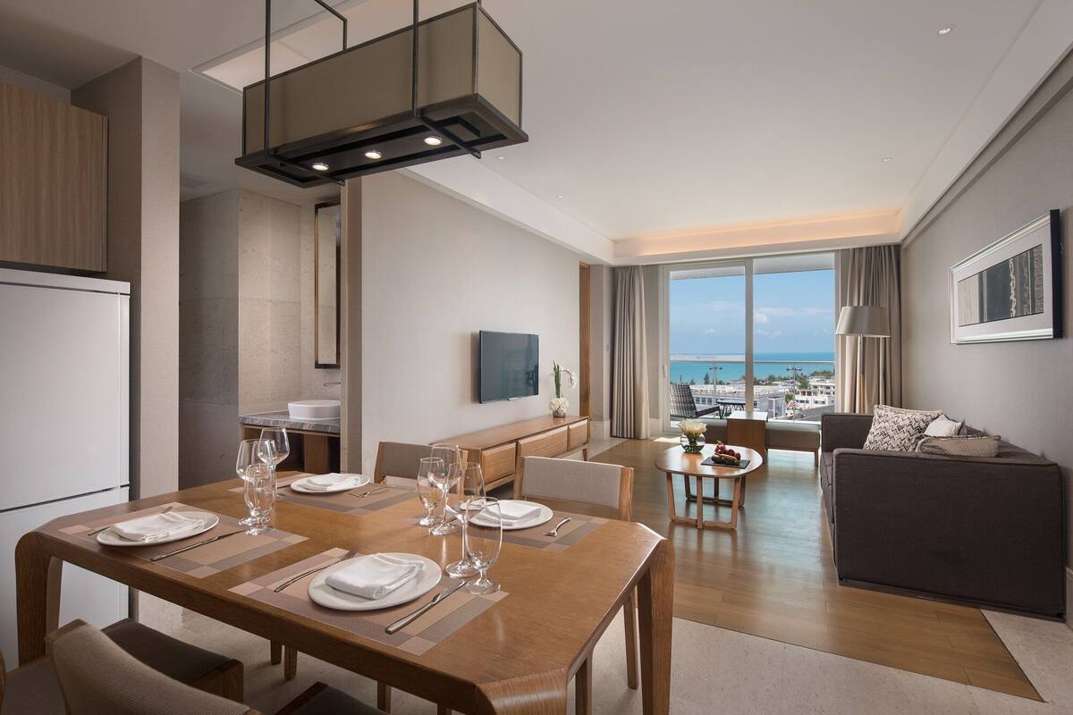 Une chambre d’hôtel moderne dotée d’un coin repas, d’un espace de vie avec vue sur la mer et d’une kitchenette.