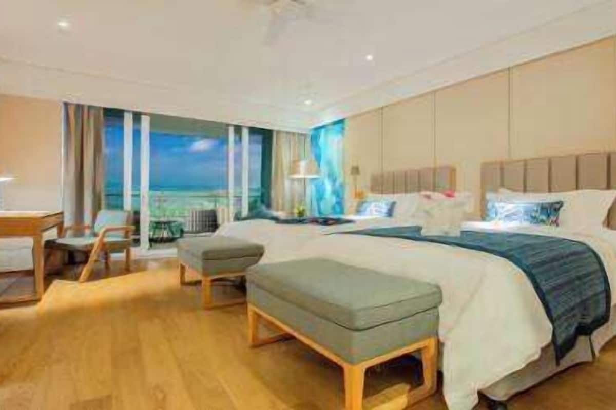 Une chambre d’hôtel moderne dotée d’un grand lit, d’un coin salon avec un fauteuil et un pouf, d’un bureau et offrant une vue sur l’océan.