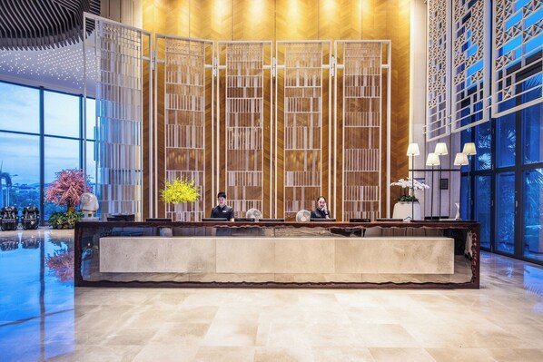 A hotel reception area with a modern design, featuring a reception desk, seating area, and large windows offering views of the cityscape.