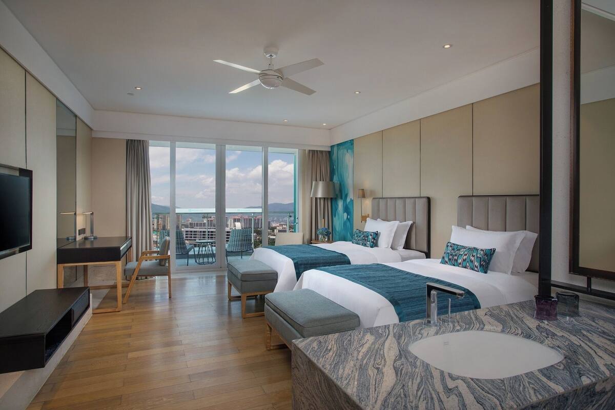 Une chambre d’hôtel moderne avec deux lits, une grande fenêtre, un bureau et une salle de bain dotée d’un comptoir en marbre.