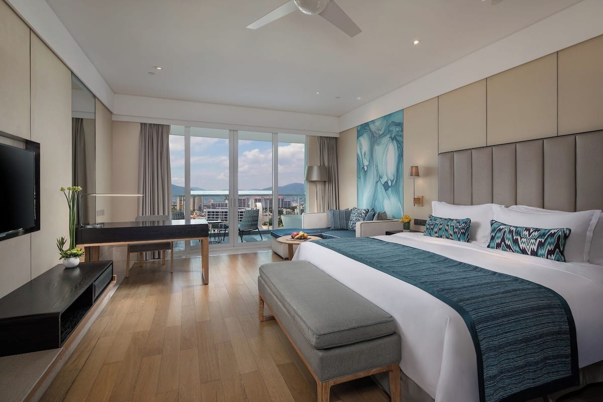 Une chambre d’hôtel moderne dotée d’un grand lit, d’un bureau et d’un balcon offrant une vue sur la ville.