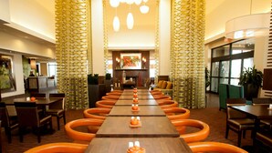 Una larga mesa de comedor con sillas anaranjadas, una chimenea y cortinas con diseños.