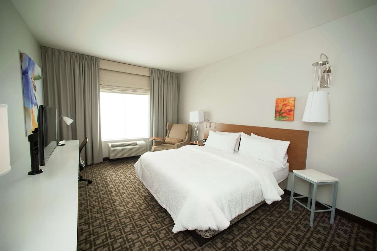 Habitación de hotel con una cama grande, un escritorio, una silla, una lámpara y un cuadro en la pared.