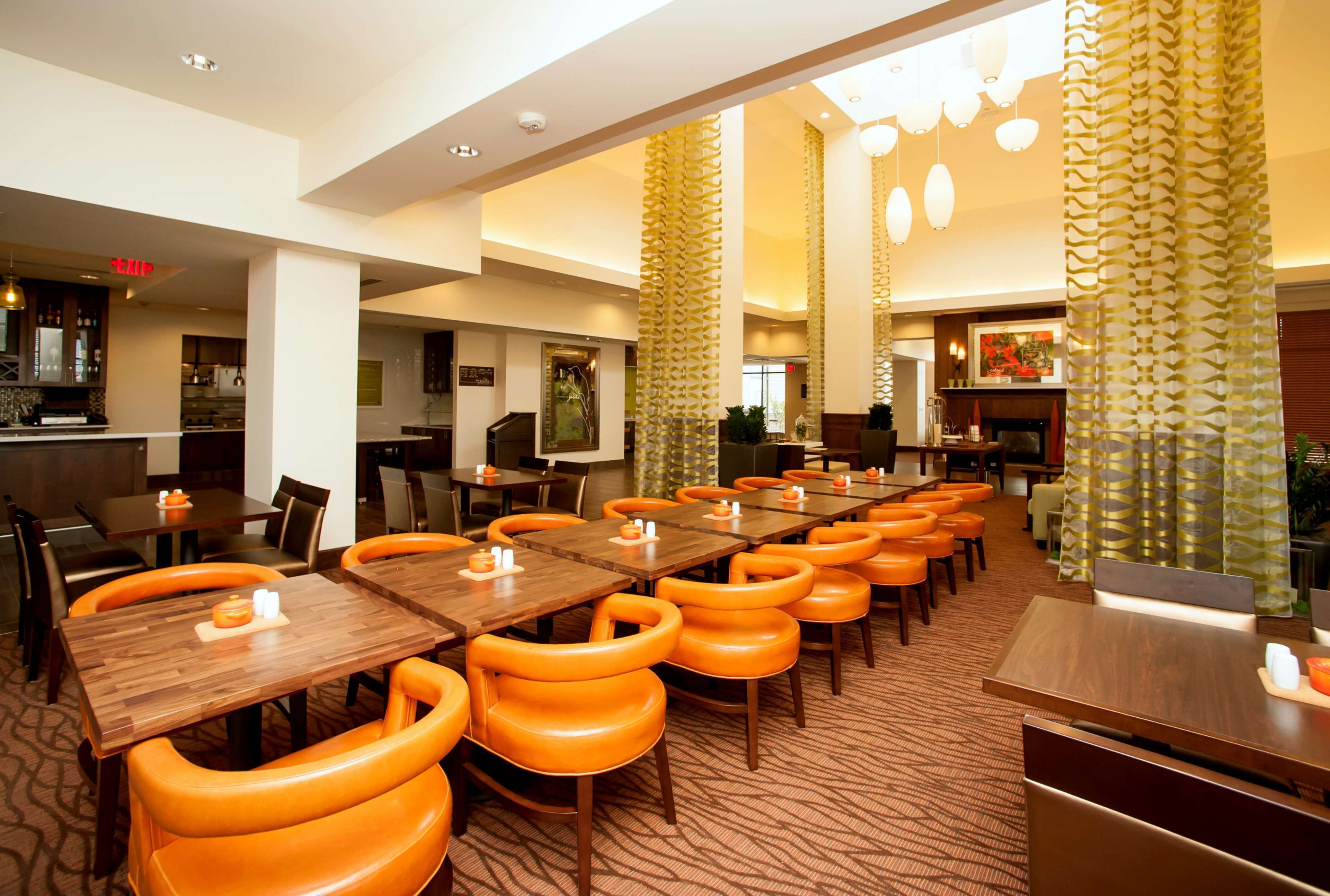A hotel dining area with multiple tables and orange chairs, a bar area, and a reception desk.