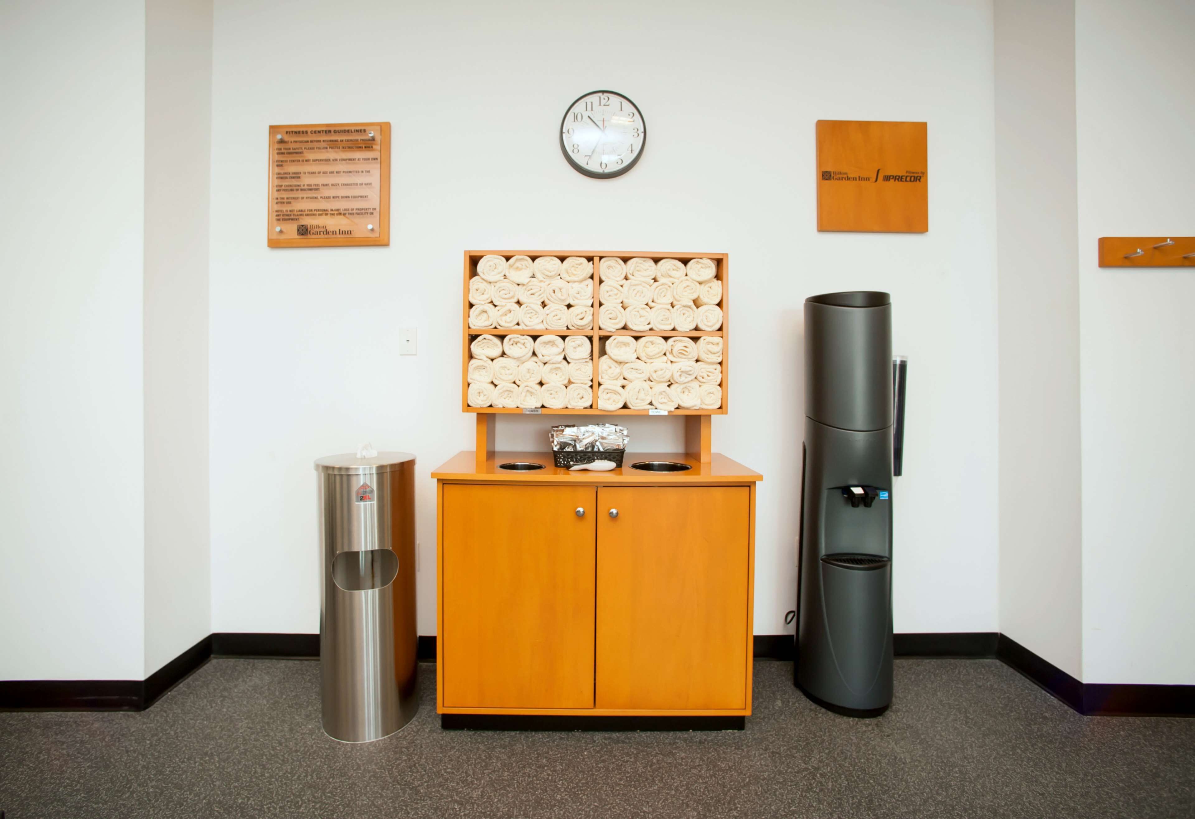 A clean, modern restroom with a wooden cabinet, a trash bin, a recycling bin, and a clock on the wall.