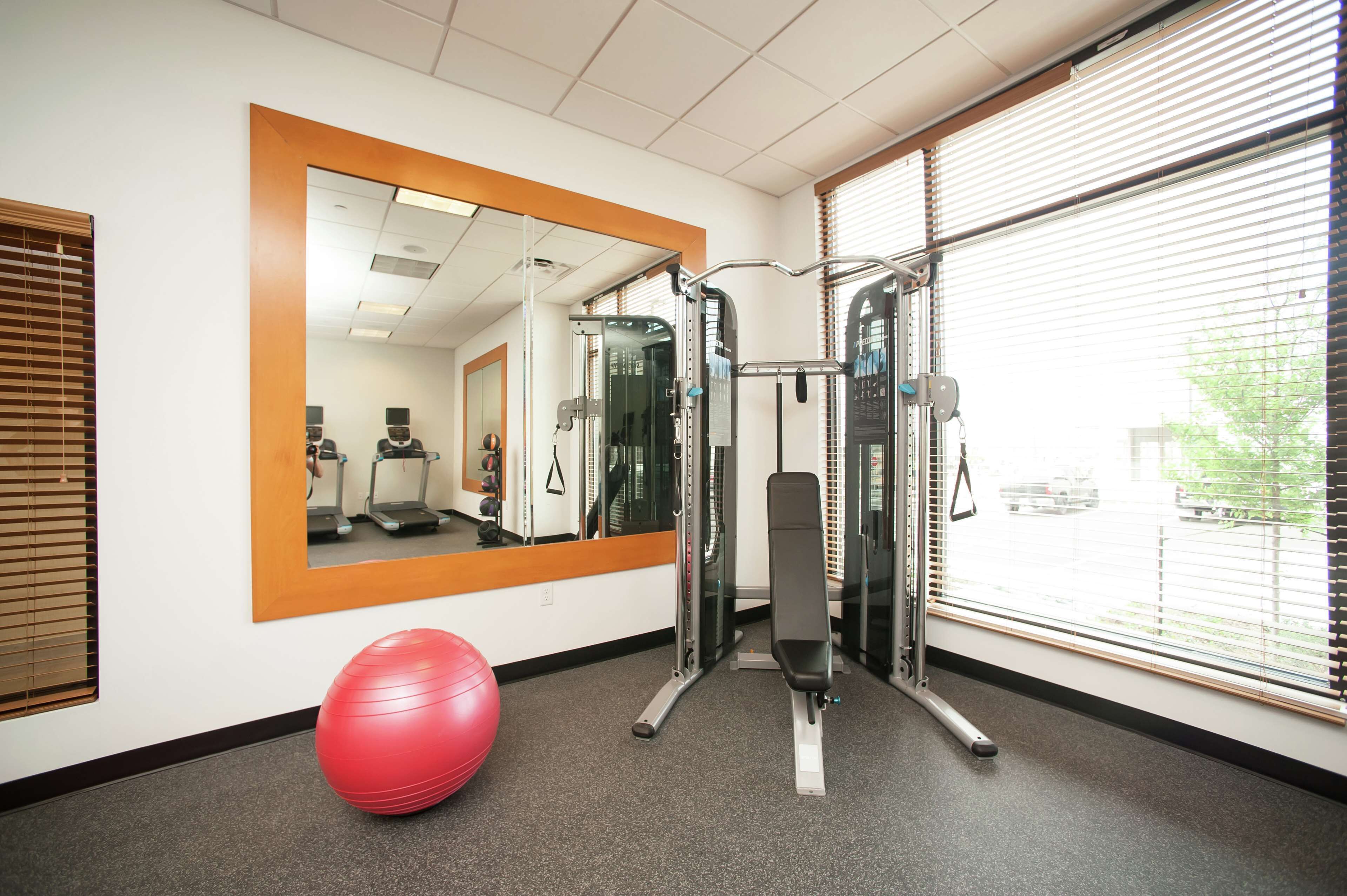 A gym with exercise equipment, a red exercise ball, and a large mirror.