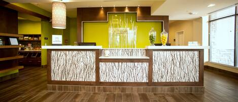 A reception area with a modern design, featuring a reception desk, a decorative wall with a tree-like pattern, and a large window providing natural light.