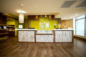 Un área de recepción con diseño moderno, que incluye un mostrador de recepción, una pared decorativa con un diseño arbóreo y un gran ventanal que proporciona luz natural.