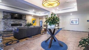 A lobby with a stone fireplace, a flat-screen TV, a gray sofa, a glass coffee table, and a large potted plant. - Creekstone Inn & Suites  (St. Marys)