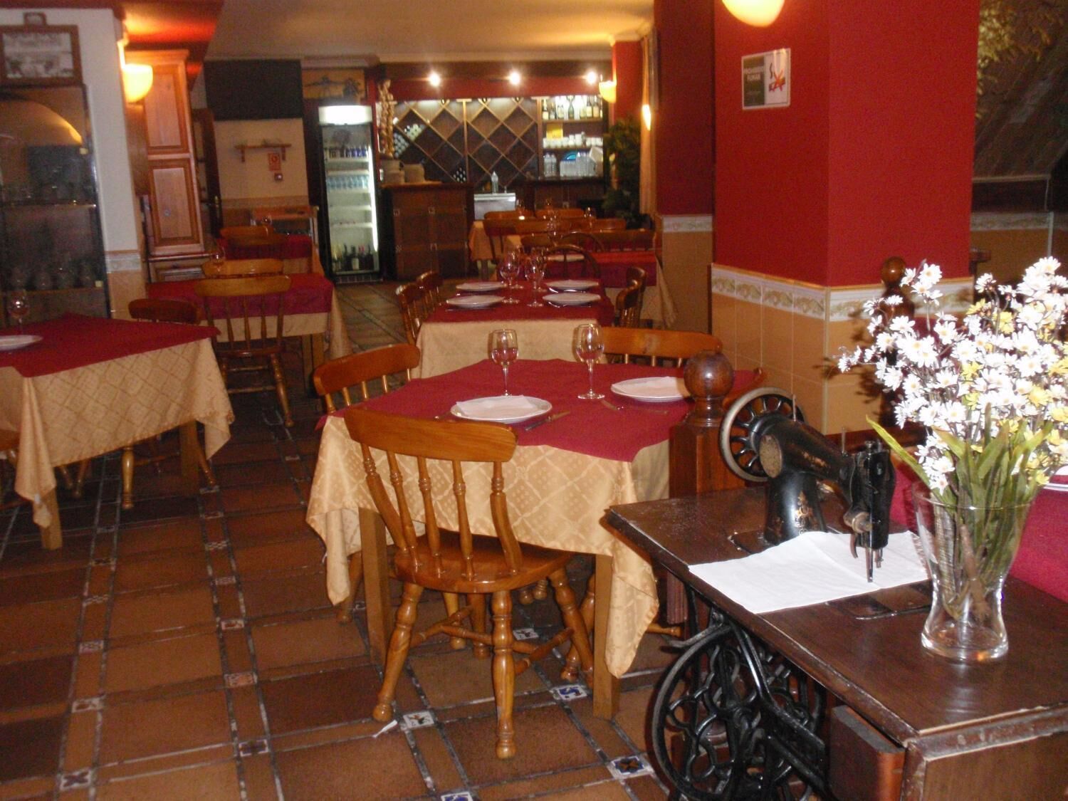 A restaurant with multiple tables set for dining, each with a red tablecloth and white plates.