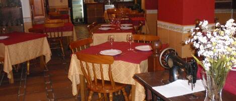 A restaurant with multiple tables set for dining, each with a red tablecloth and white plates.