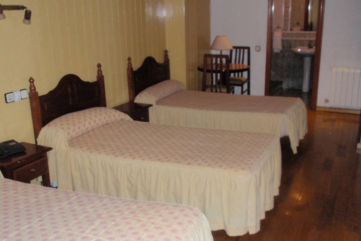 Une chambre d’hôtel avec deux lits simples, une table de chevet en bois, une chaise et une salle de bain équipée d’un lavabo et d’un miroir.