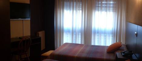 A hotel room with two beds, a desk, a chair, a television, and a window with curtains.