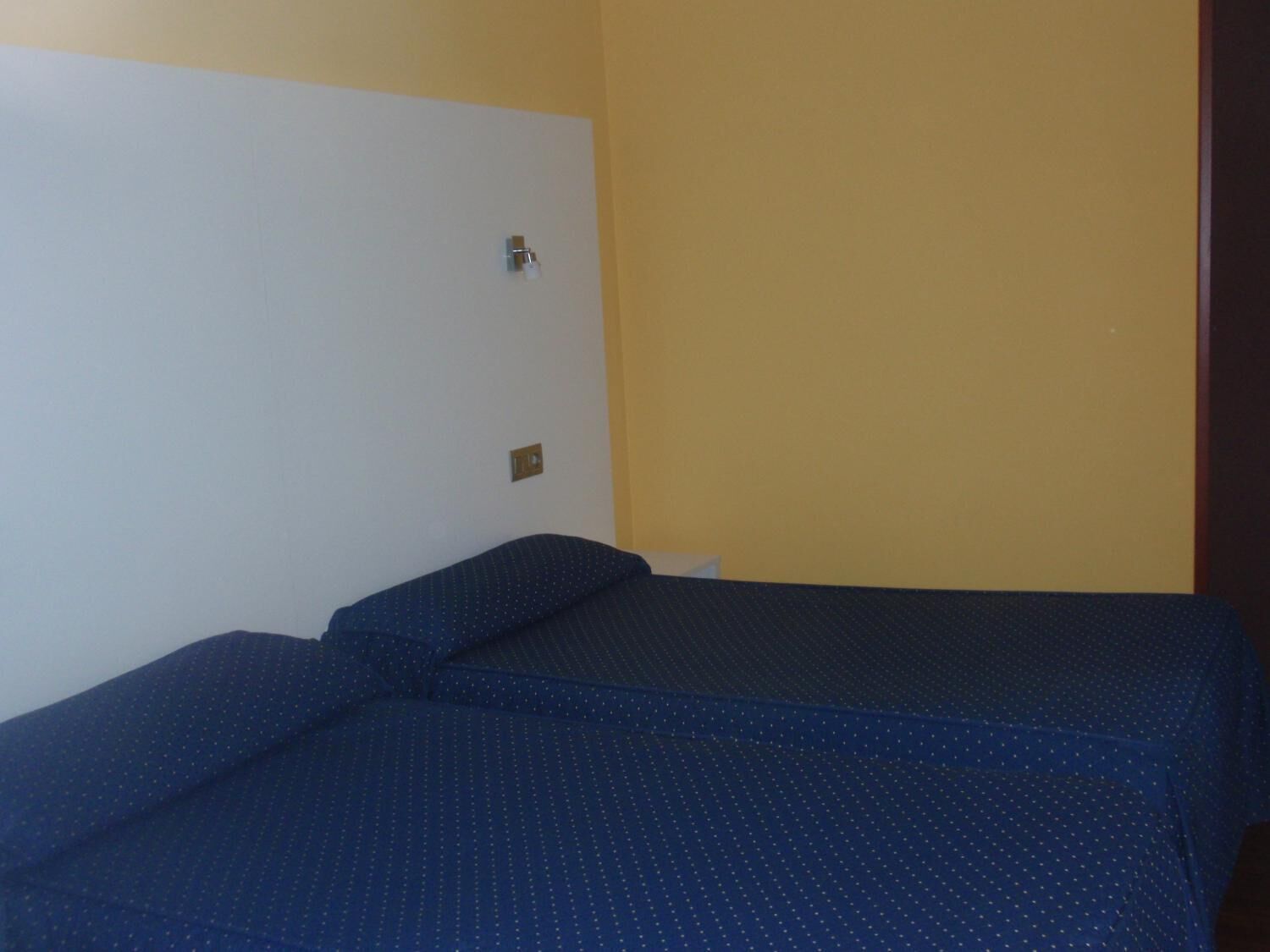Una habitación con dos camas, una pared blanca y otra amarilla.