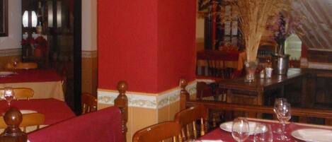 A dining area with red walls and wooden chairs. Tables are set with white plates, glasses, and cutlery.