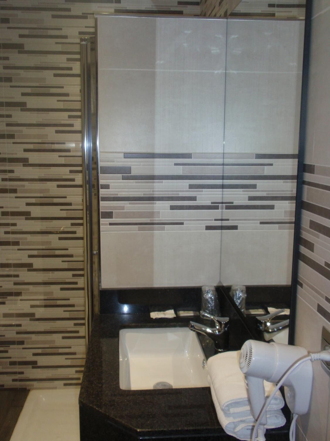 A bathroom with a modern design, featuring a large mirror, a sink, and a hairdryer on the counter.