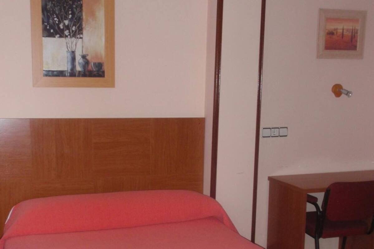 Un lit simple avec une tête de lit en bois, un bureau avec une chaise et deux œuvres d’art encadrées accrochées au mur.
