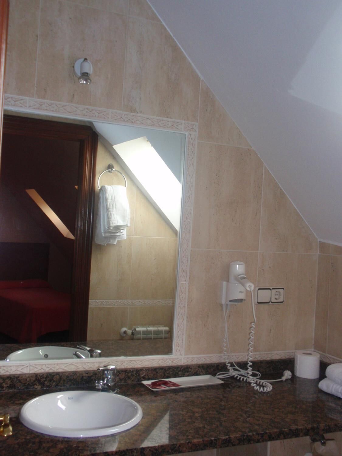Een badkamer met een wastafel, spiegel, handdoekhouder en een föhn aan de muur.