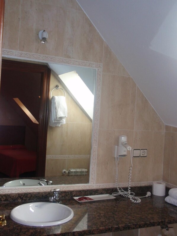 Un baño con lavamanos, espejo, toallero y secador de pelo en la pared.