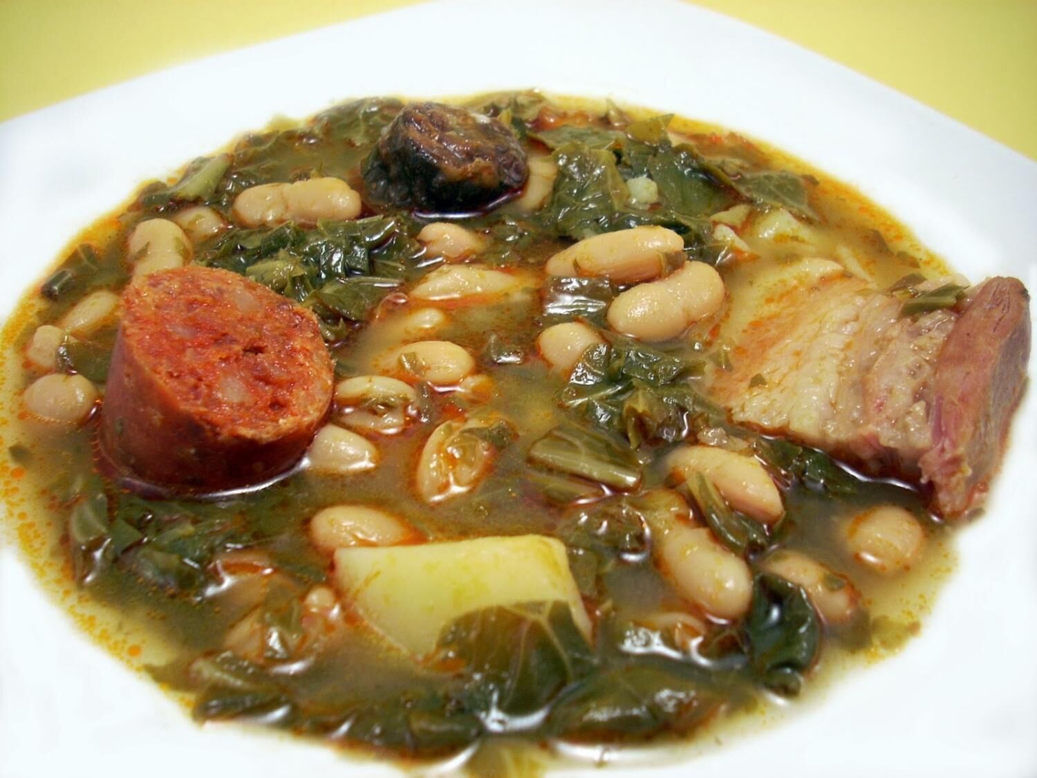 Um prato de ensopado com feijão, linguiça e vegetais.