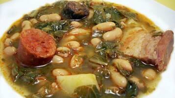 Um prato de ensopado com feijão, linguiça e vegetais.