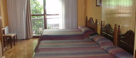 A hotel room with two beds, a wooden headboard, a small desk with a chair, and a window with curtains.
