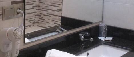 Un baño moderno con encimera negra, lavabo blanco, secador de pelo y toalla.