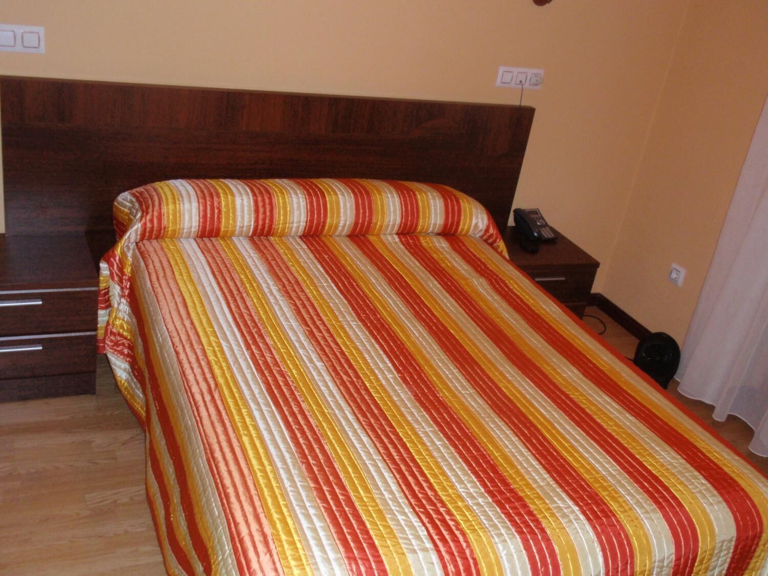 A bed with a striped bedspread in a room with a wooden headboard and a bedside table with a phone.