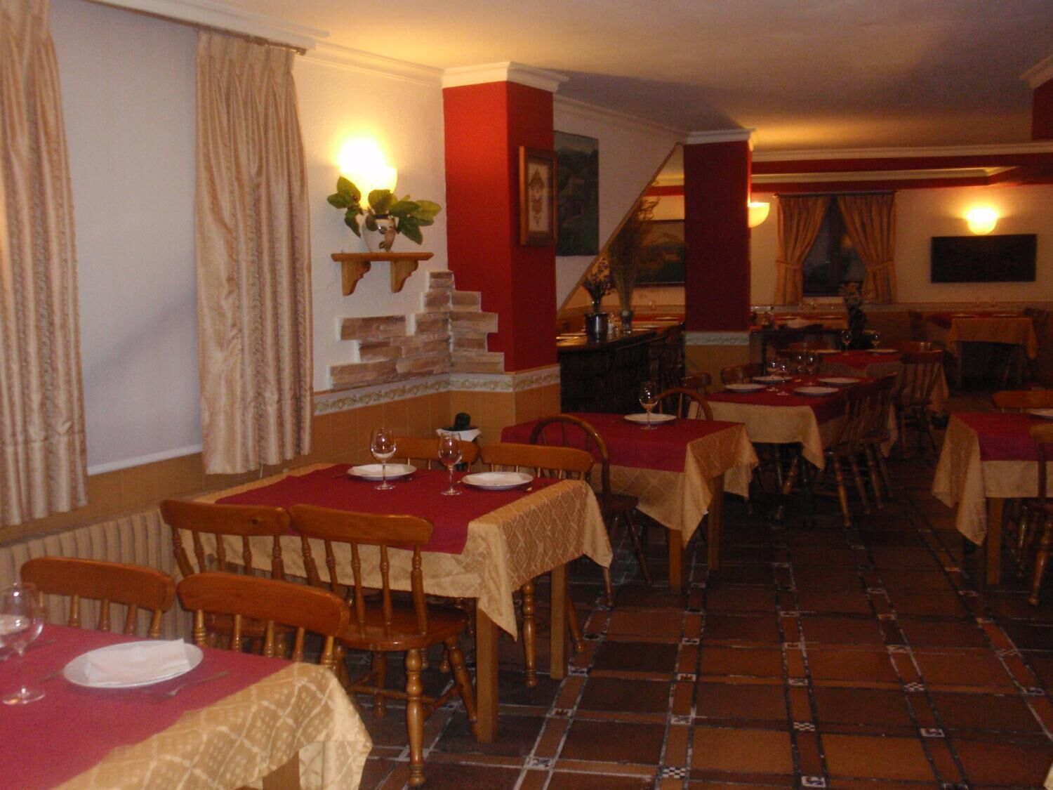 Un restaurante con varias mesas y sillas, una escalera y un estante en la pared con una planta.
