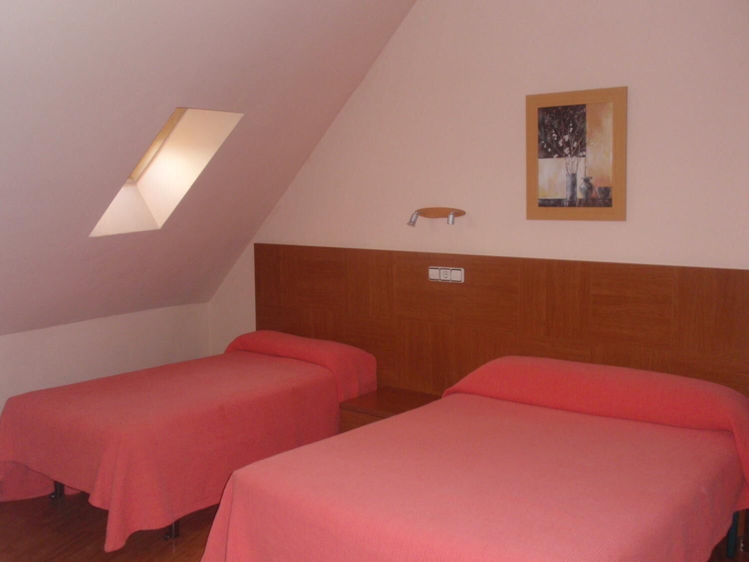 A room with two beds, a skylight, a painting, and a small table with a light fixture.