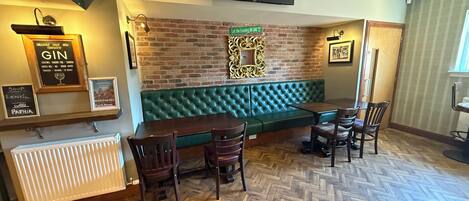 Un rincón de bar acogedor con un banco acolchado verde, sillas de madera y un suelo con estampado de espiga.