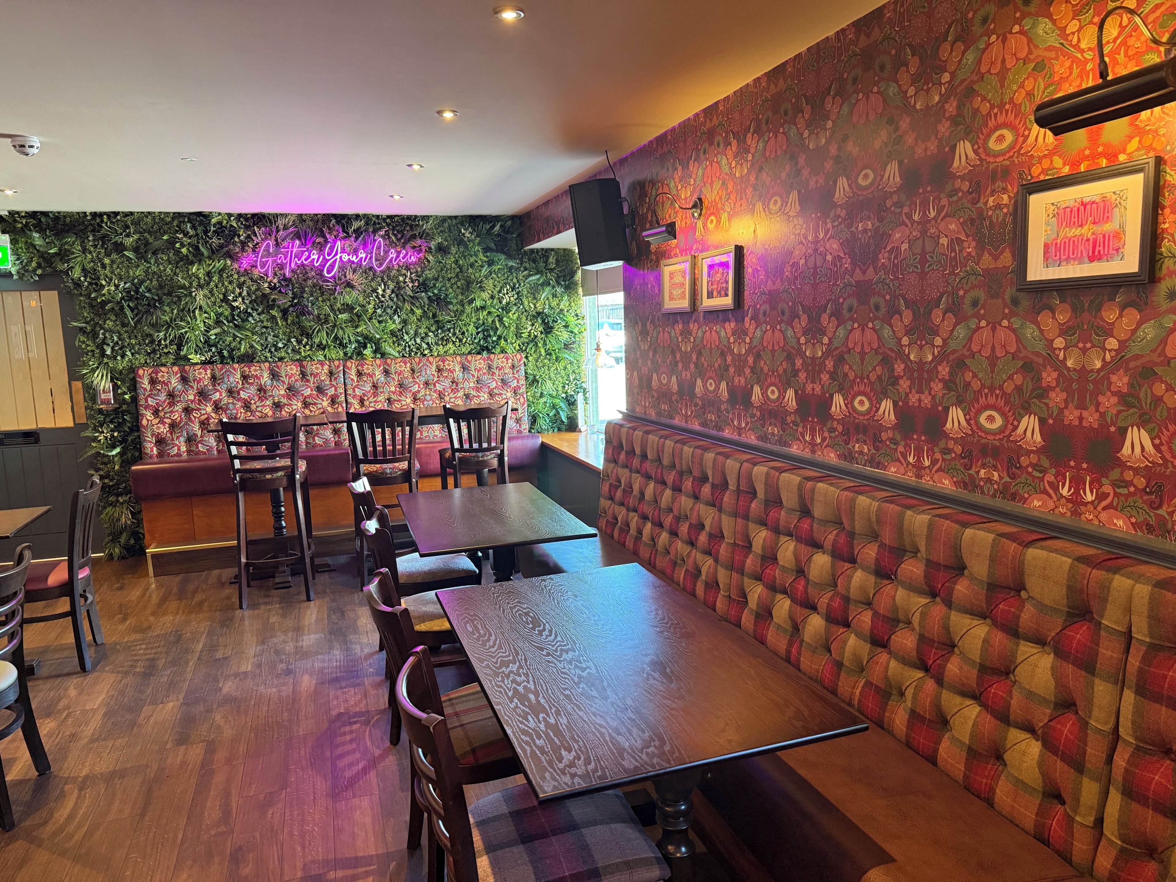 A restaurant interior with wooden tables and chairs, a neon sign, and a mural on the wall.