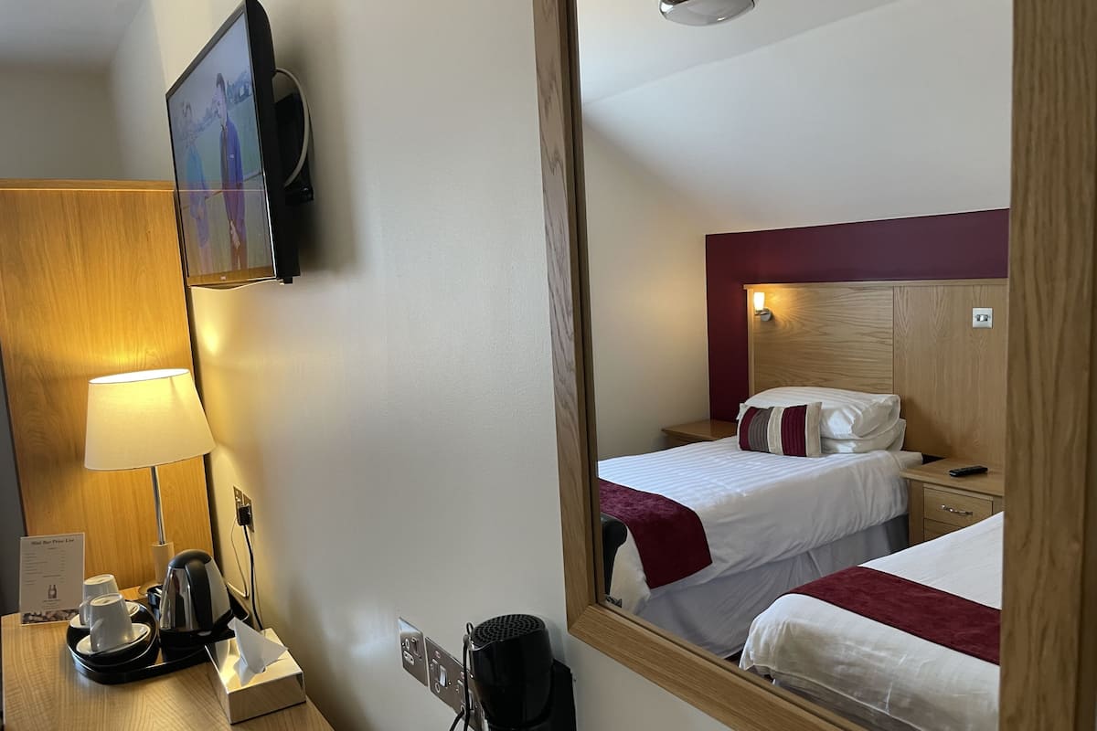 A hotel room with a bed, bedside table, lamp, and a mirror reflecting the room.
