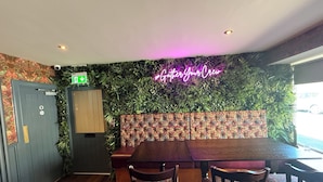 A restaurant interior with a neon sign, wooden furniture, and a green wall with plants. - 19th Hole Hotel (Carnoustie)