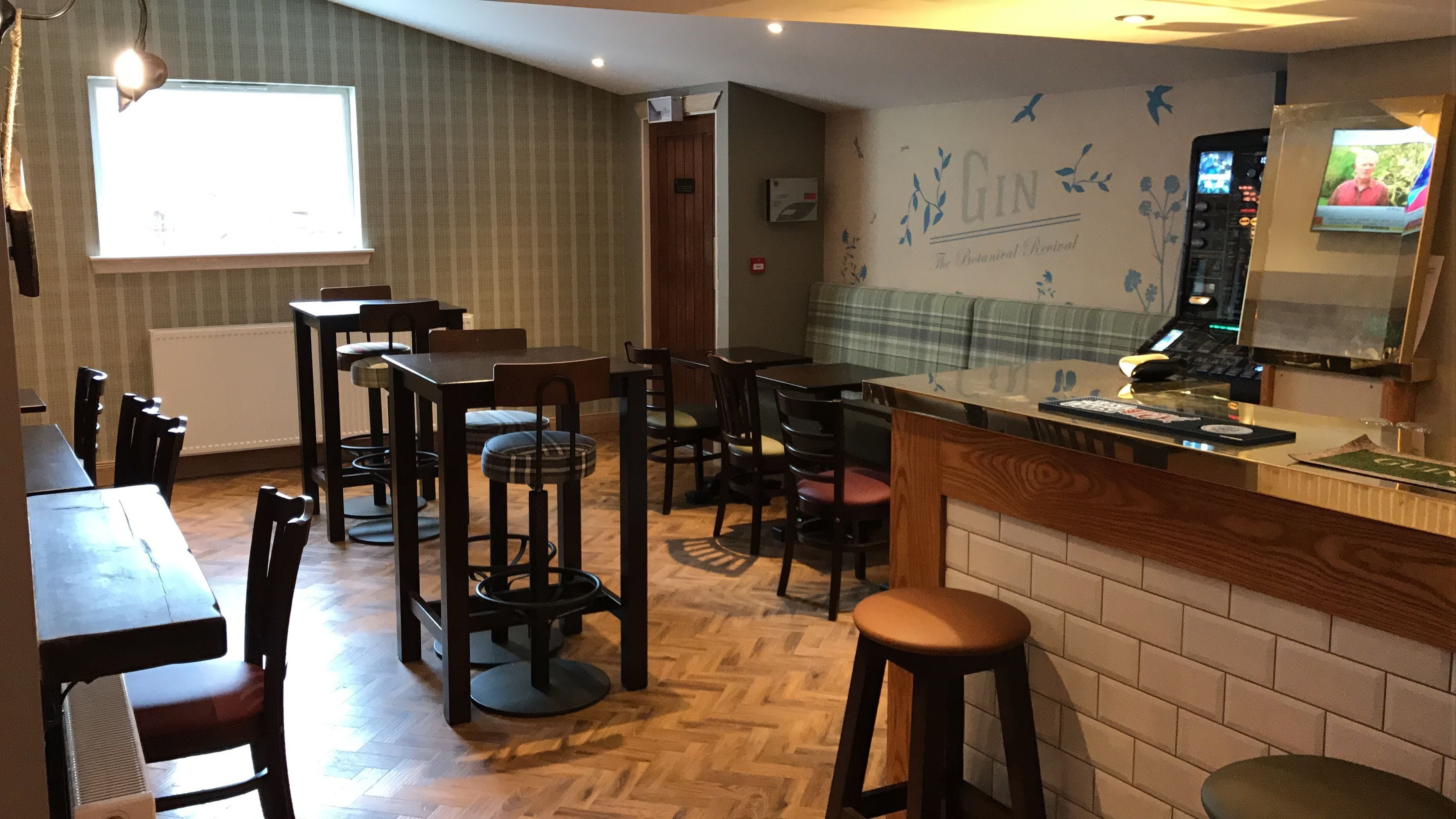 A restaurant with a wooden herringbone floor, a bar area with stools, and a wall with a botanical design.