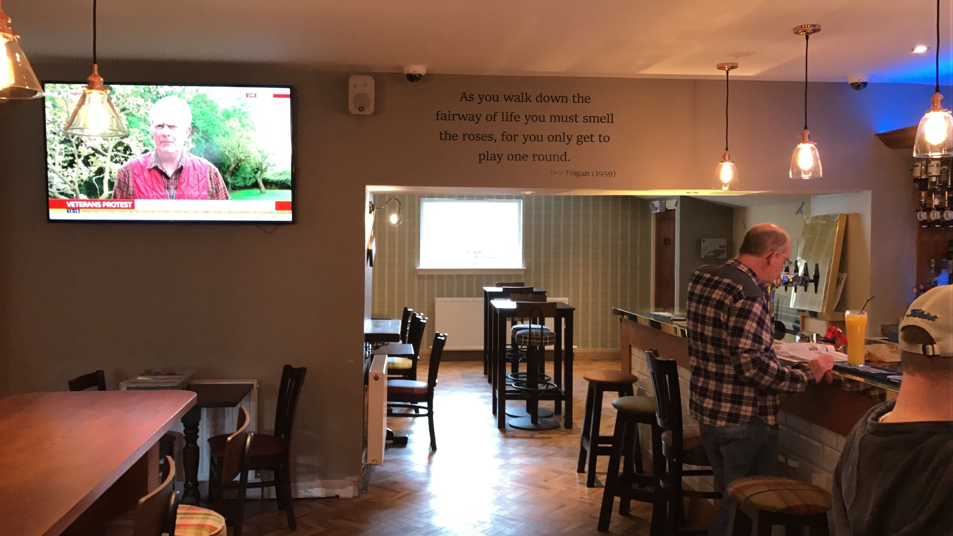Un restaurante con una televisión mostrando un noticiero, una cita en la pared y una zona de bar.
