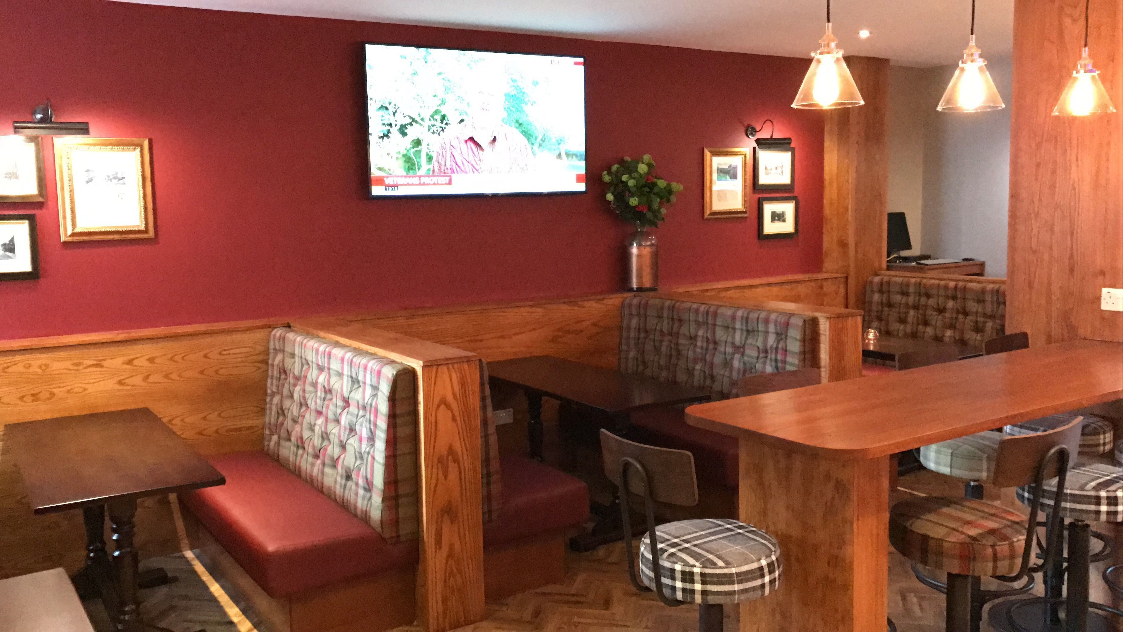 A restaurant with booths and tables, wooden flooring, and a television on the wall.