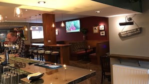 A bar area with a polished bar counter, stools, and a television mounted on the wall. - 19th Hole Hotel (Carnoustie)