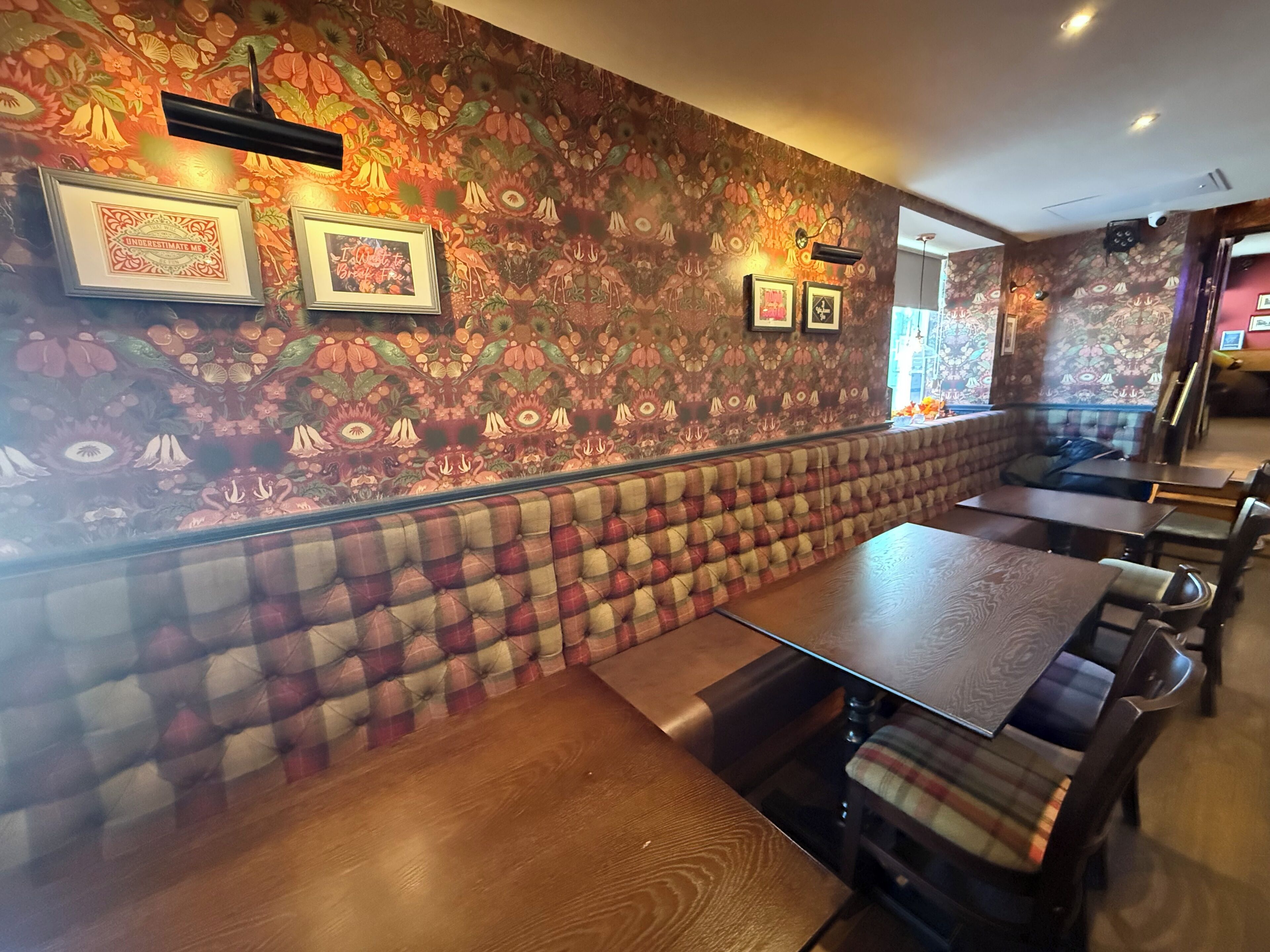 A restaurant interior with a patterned wall, cushioned seating, and framed artwork.