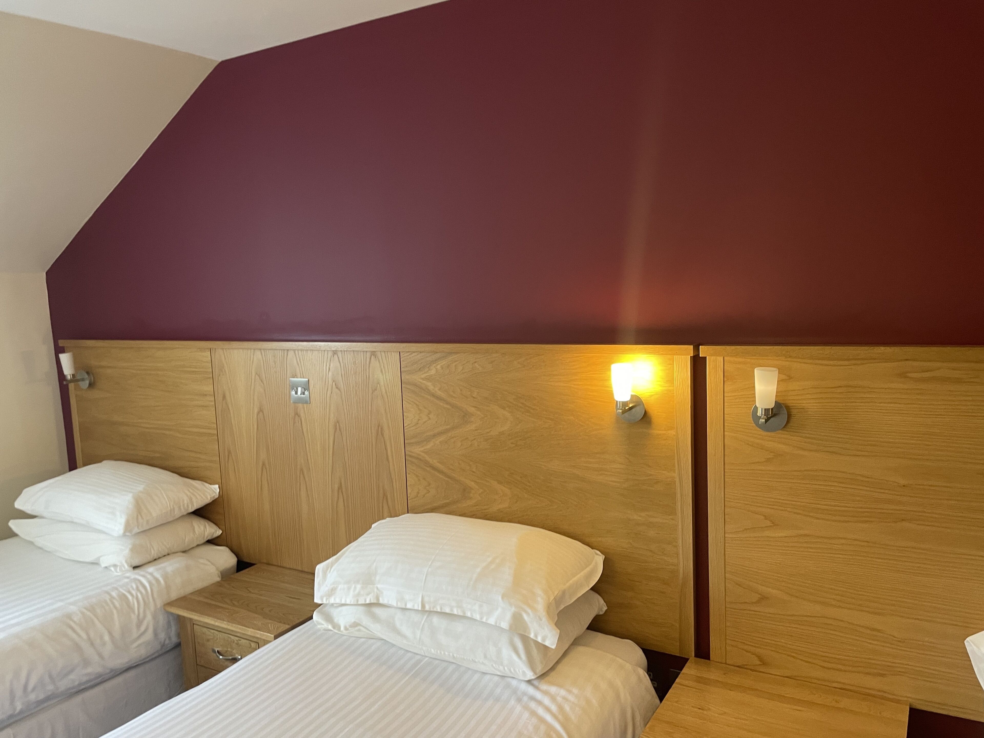 A hotel room with two beds, wooden headboards, and wall-mounted light fixtures.
