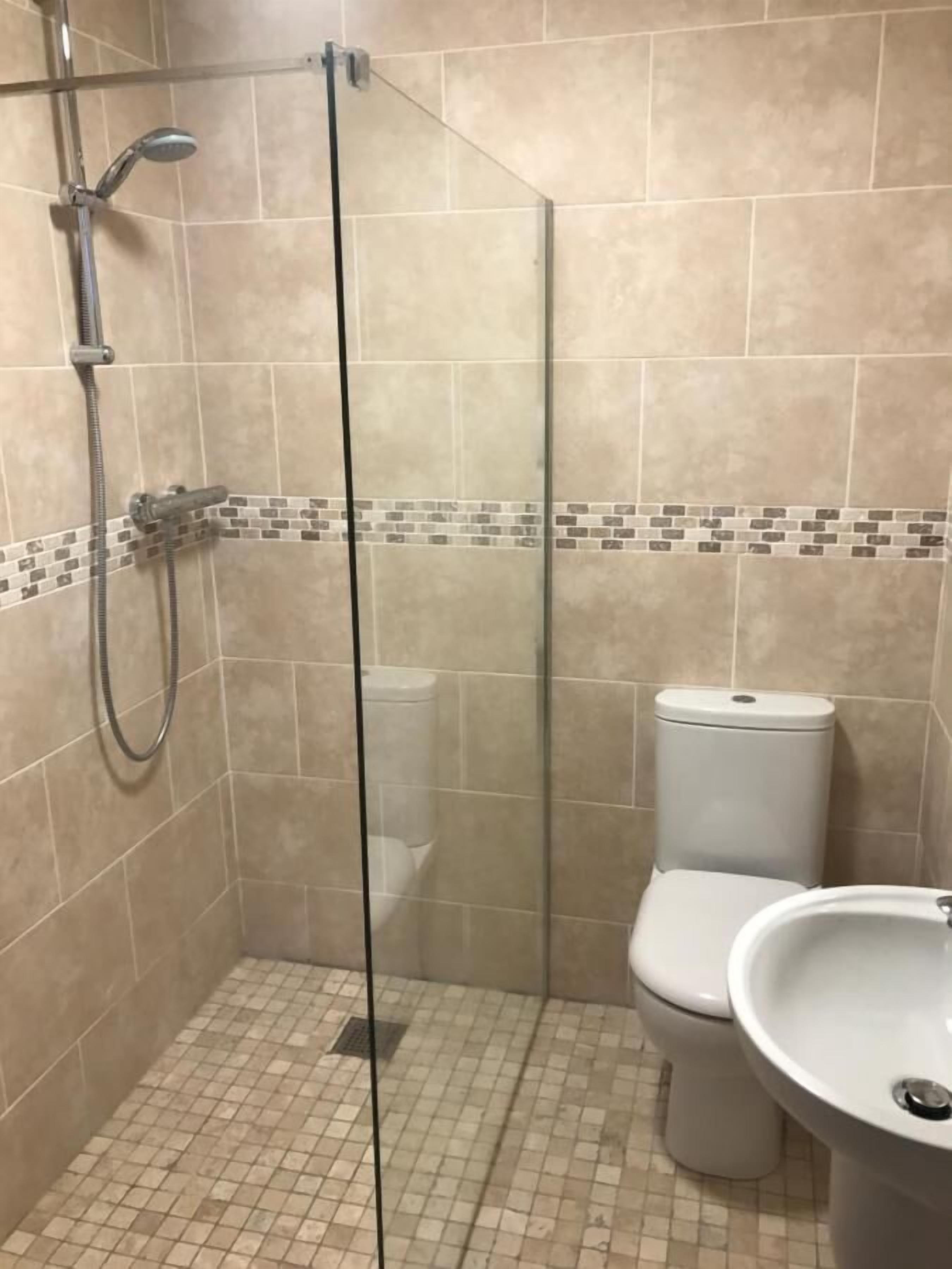 Une douche fermée par des parois en verre, dotée d’un pommeau de douche à main et d’un robinet mural.