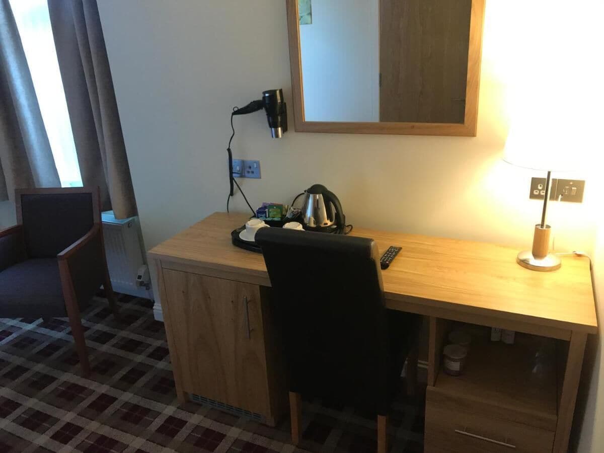 Ein kleines, ordentliches Zimmer mit einem Holztisch, einem Stuhl, einer Lampe und einem Spiegel.