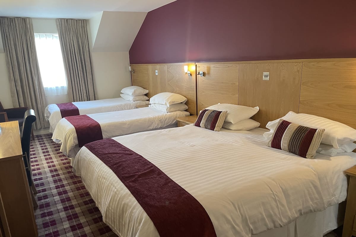 A hotel room with three beds, a wooden headboard, a checkered floor, and a window with curtains.