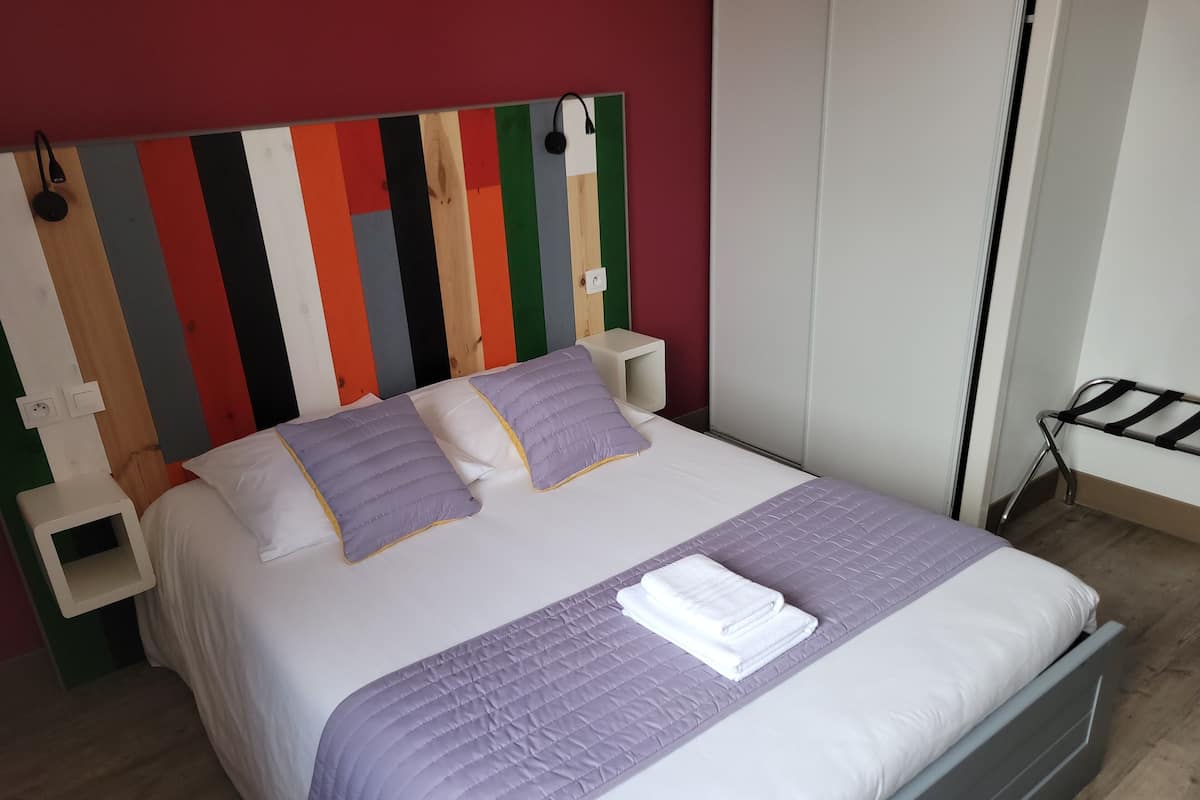 A neatly made bed with a purple quilt, two pillows, and a folded white towel.